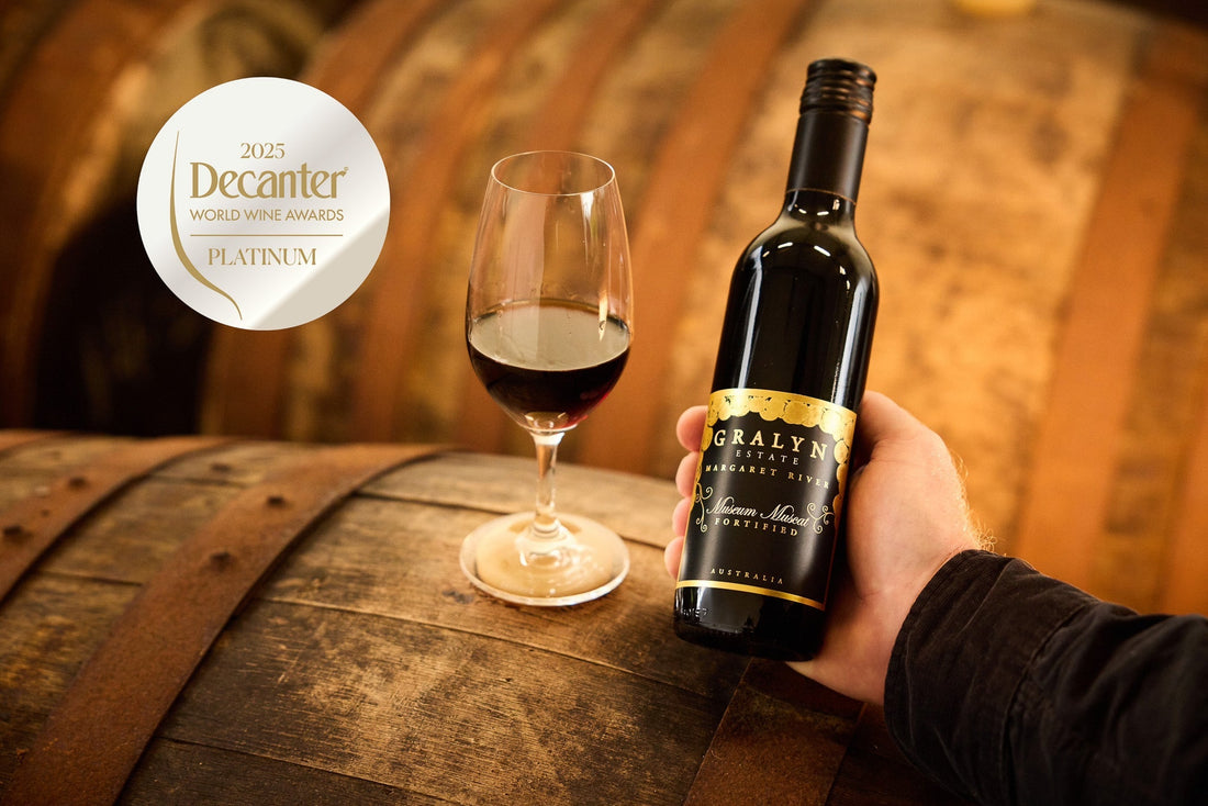 Bottle of Gralyn Estate Museum Rare Muscat beside a glass of fortified wine on a barrel, with 2025 Decanter World Wine Awards Platinum Medal badge overlay.